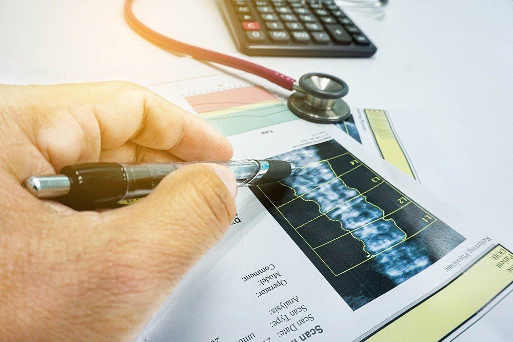 Hand holding pen pointing at spinal X-ray with calculator and stethoscope on a table.