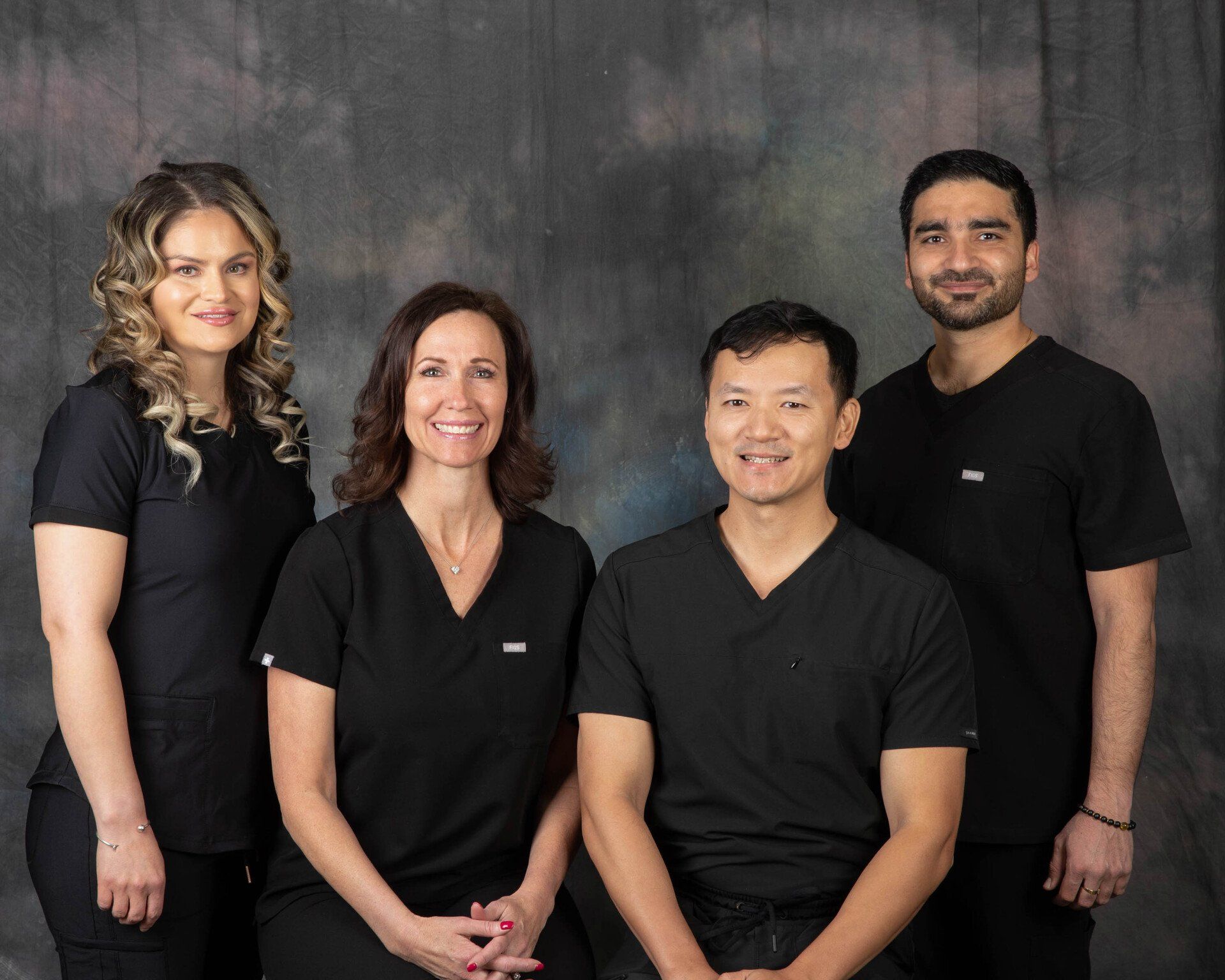 Four healthcare professionals in black scrubs posing for a group photo.