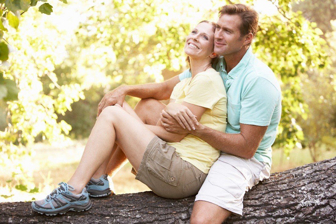 Couple sitting on a log, smiling and embracing in a sunlit park.