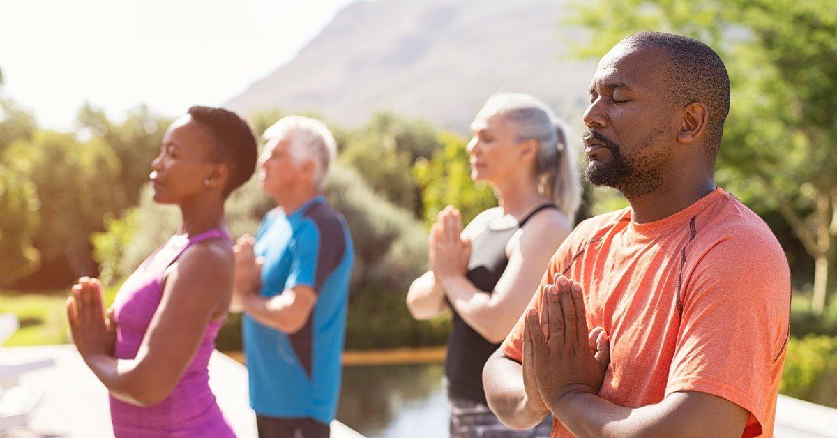 Group of people outdoors practicing yoga with hands together in prayer.