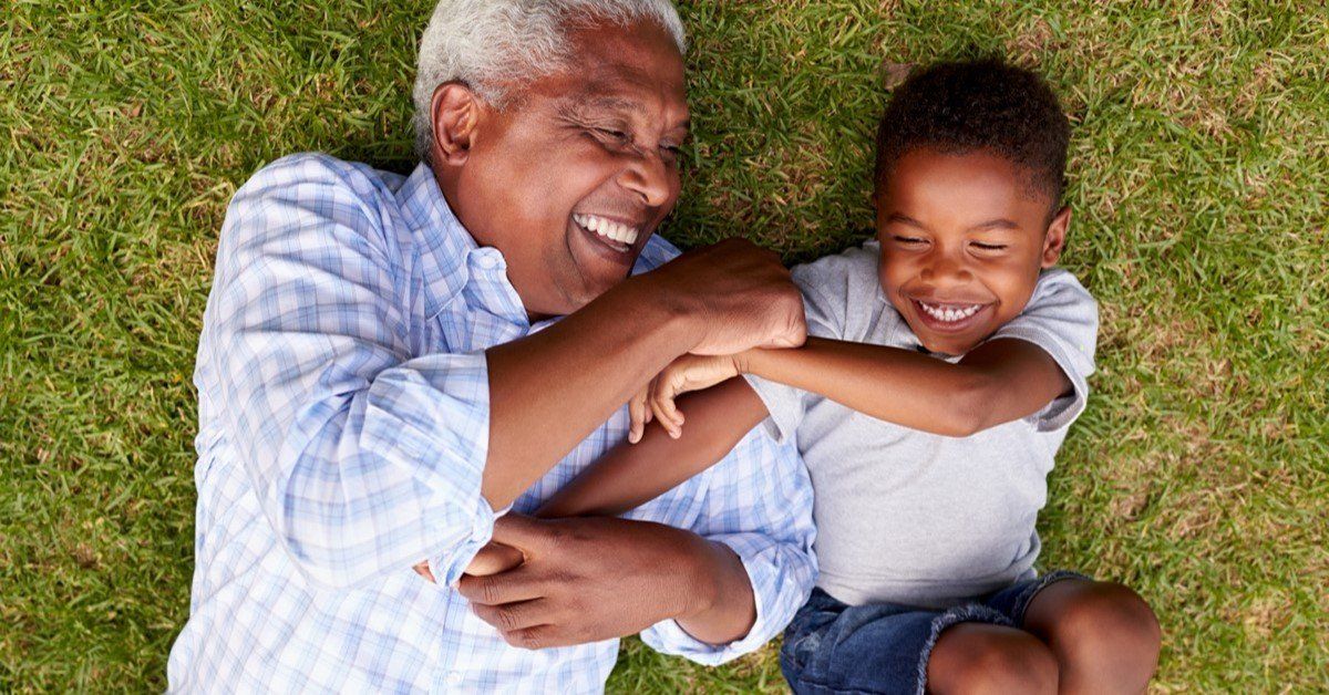 Grandfather and grandson laughing, lying in grass.