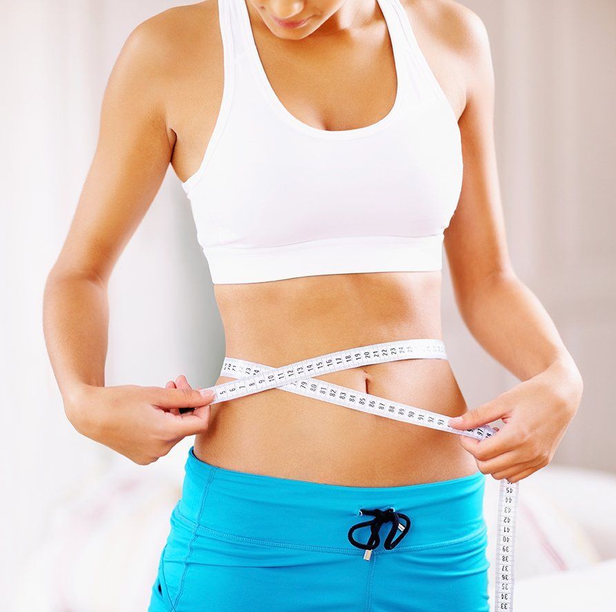 Woman in workout clothes measures waist with a tape measure.