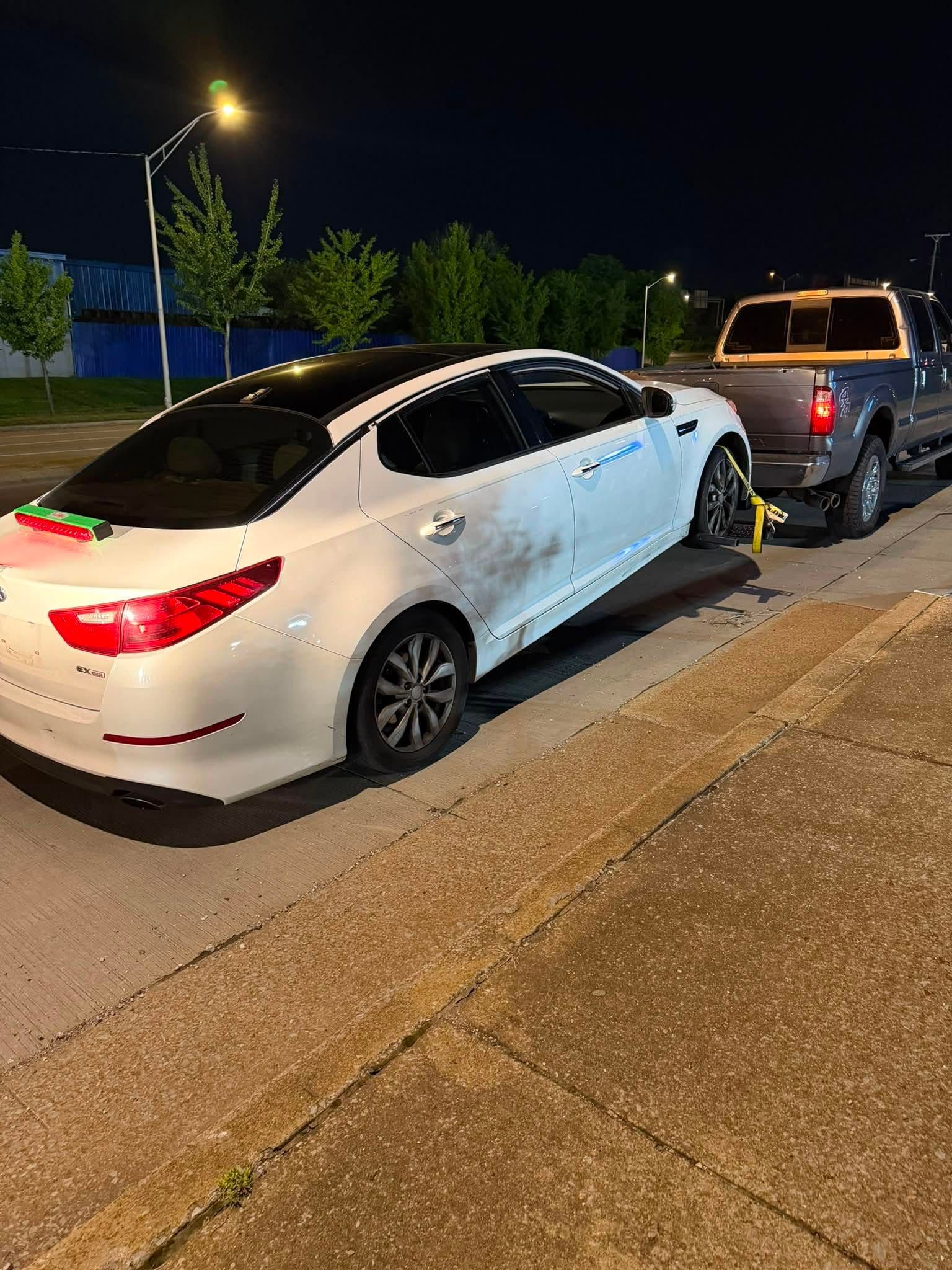 White sedan with side damage parked behind a dark pickup on a city street at night