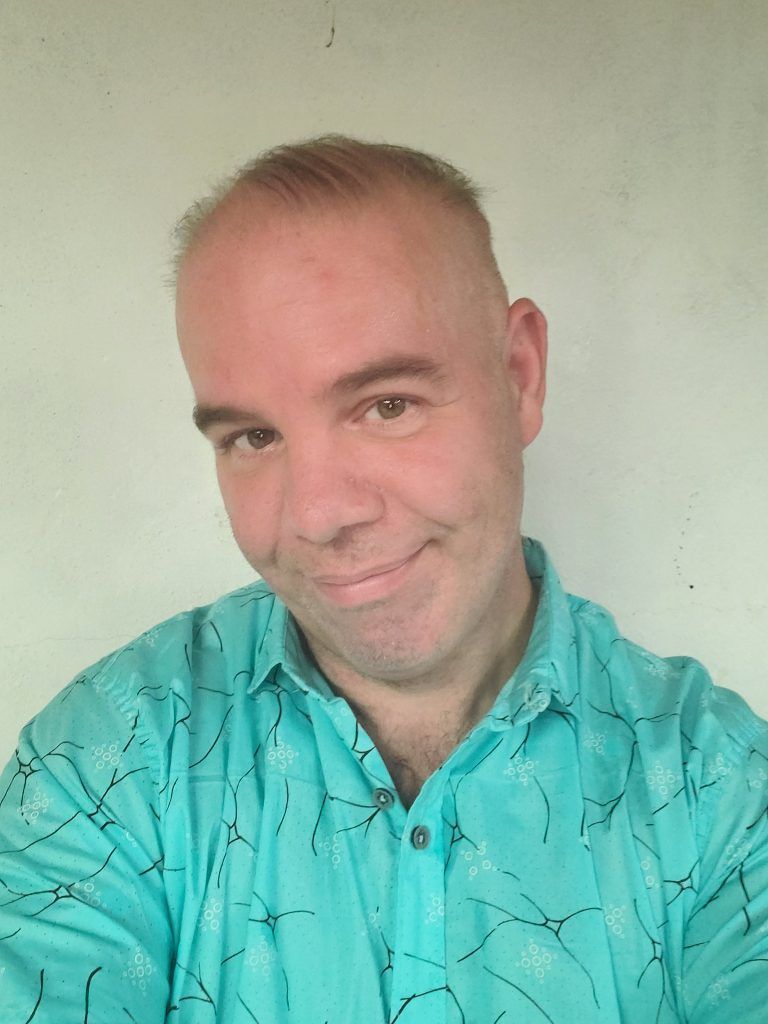 A man in a blue shirt is smiling and taking a selfie.