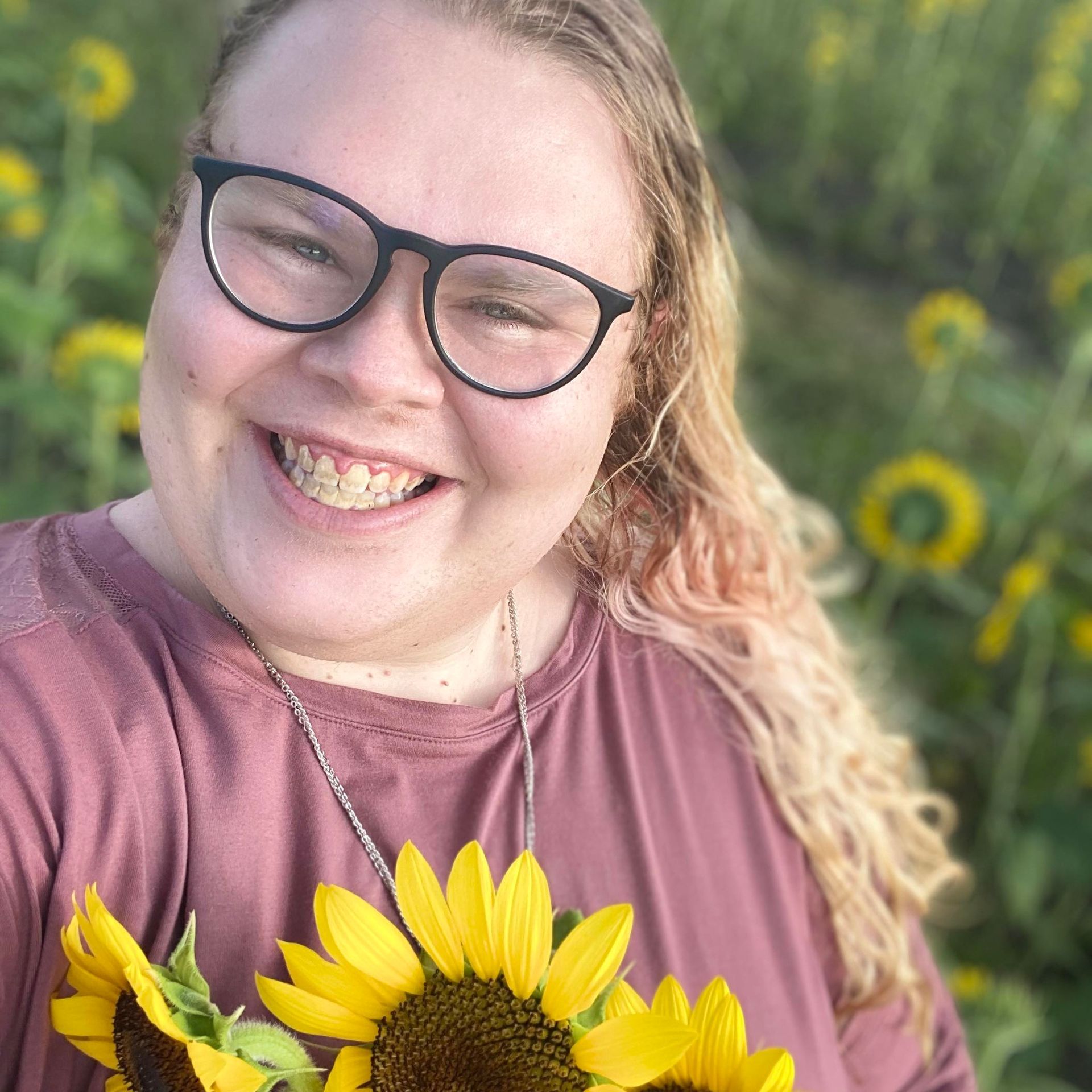 A person wearing glasses is holding a sunflower and smiling.