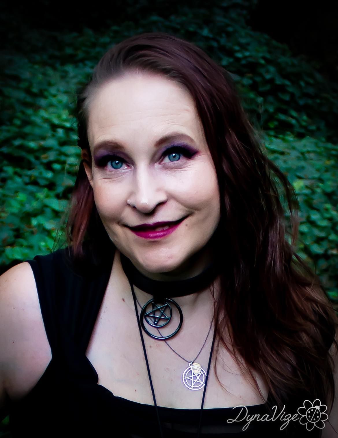 A person wearing a black top and a pentagram necklace is smiling for the camera.