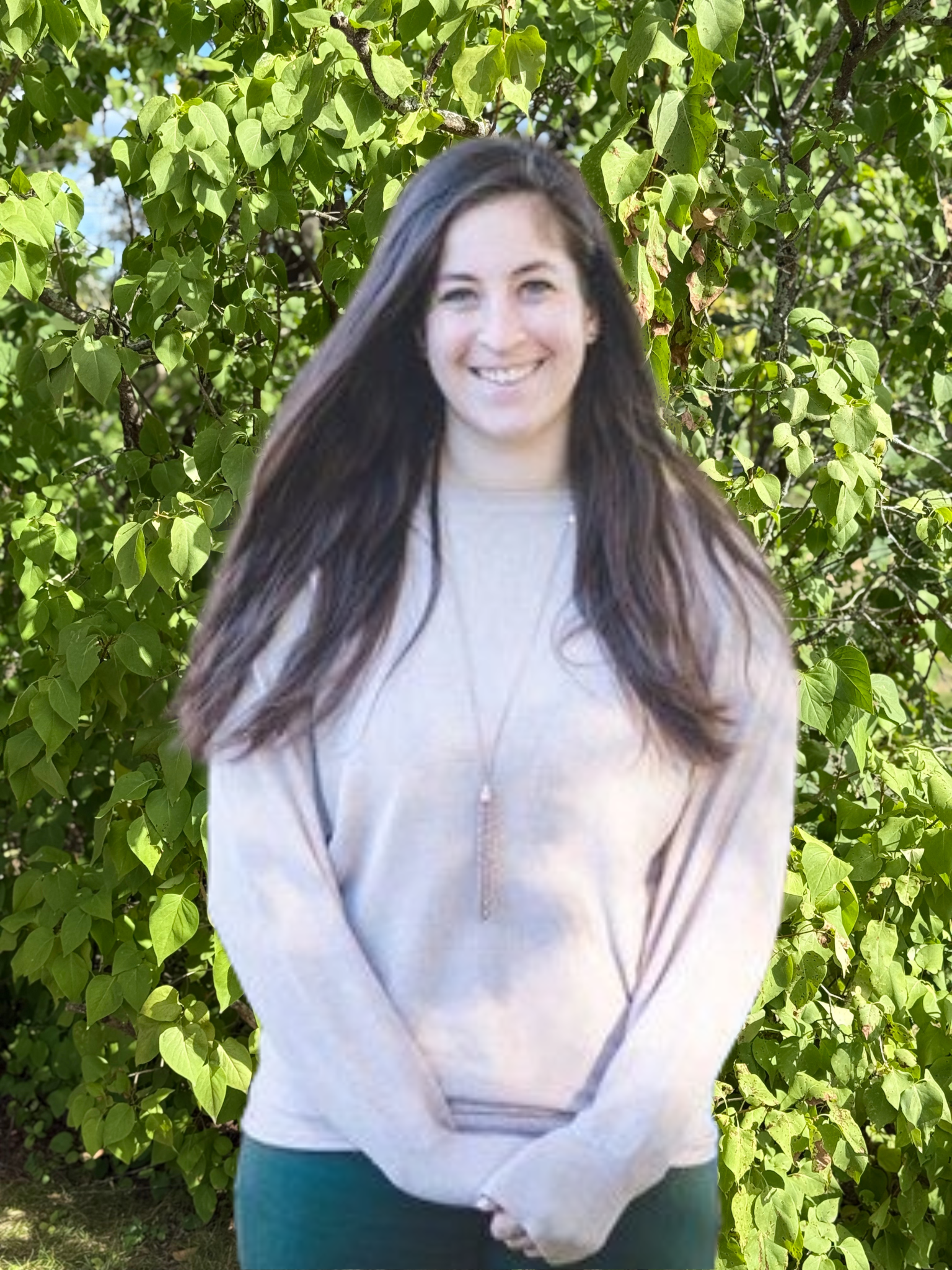 A woman in a sweater is standing in front of a tree.