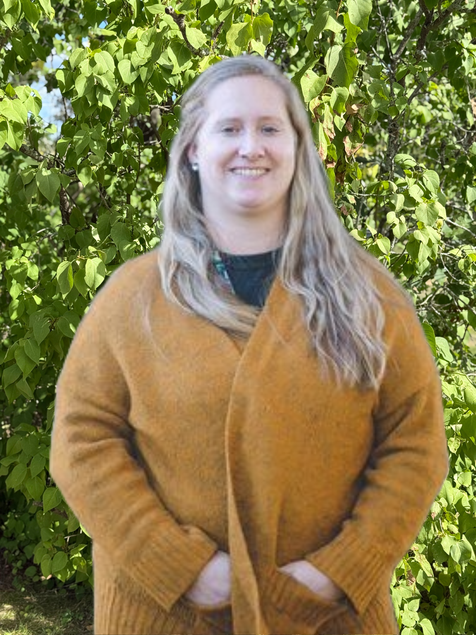 A woman in a yellow sweater is standing in front of a tree.