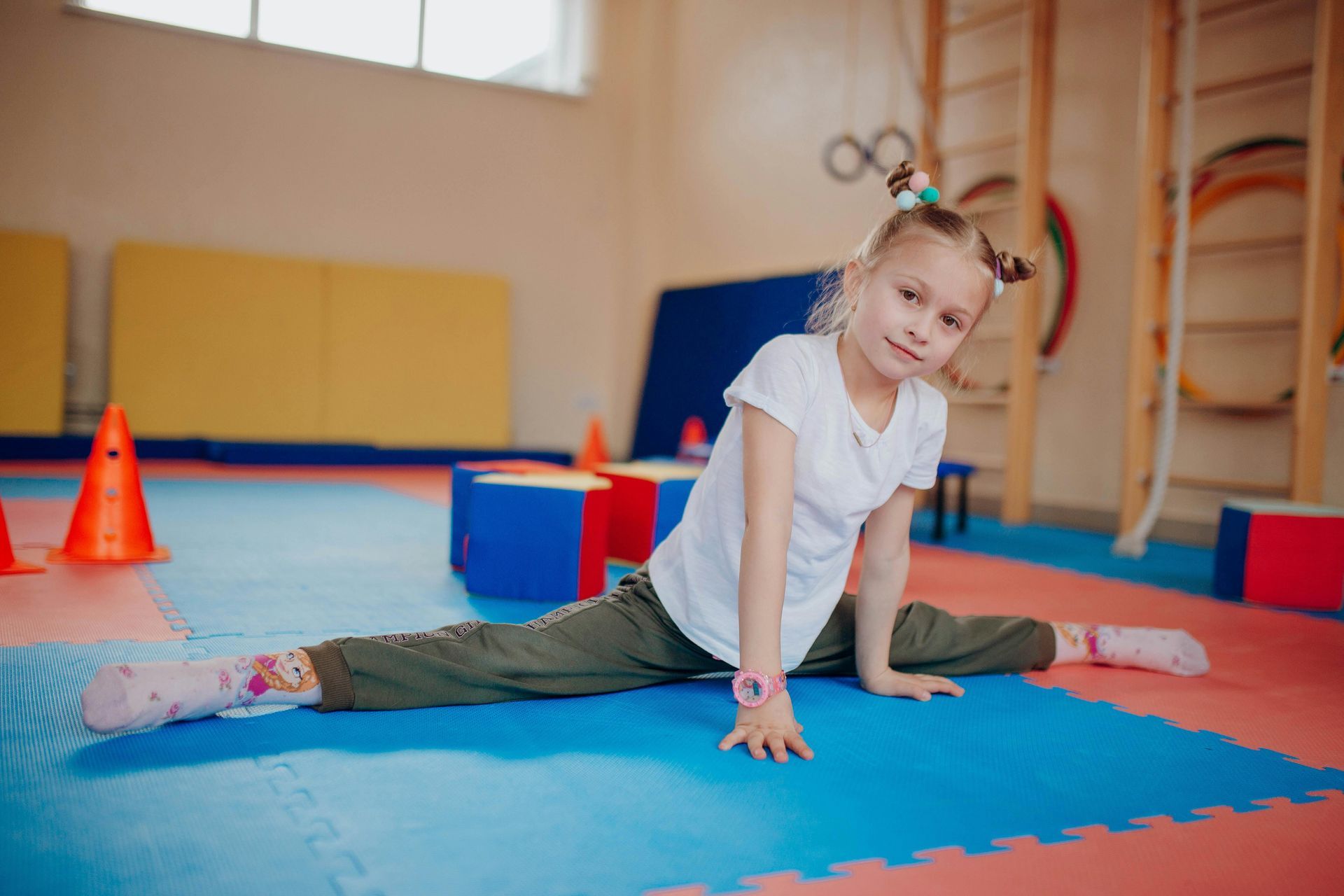 A little girl is doing a split on the floor in a gym.