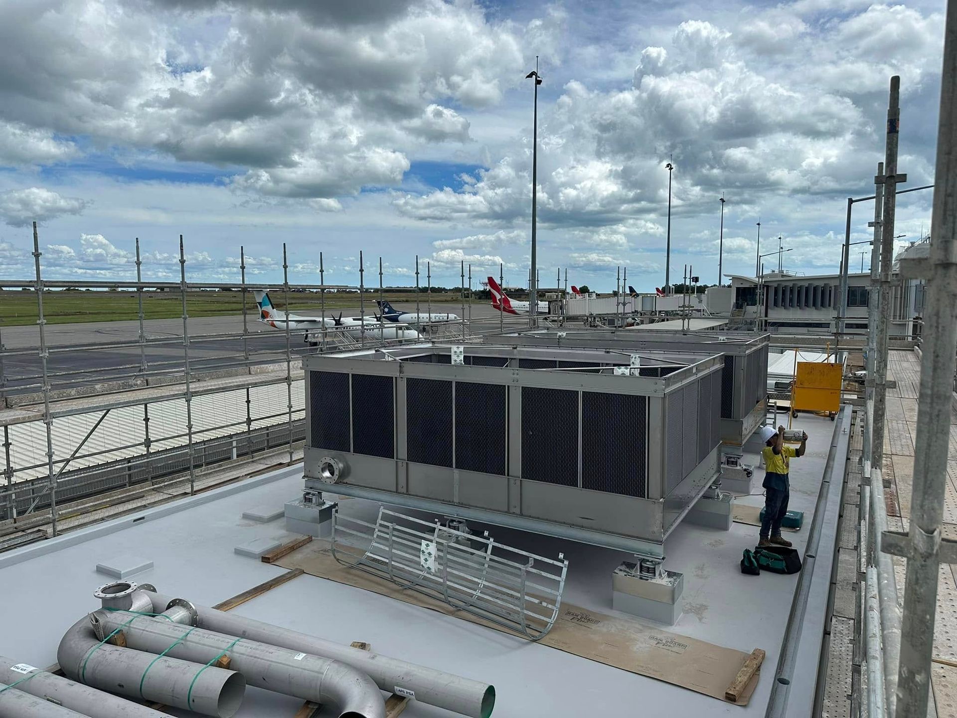Large rooftop air conditioning units at an airport, with workers and scaffolding — Great Northern Airconditioning & Mechanical Services in Berrimah, NT