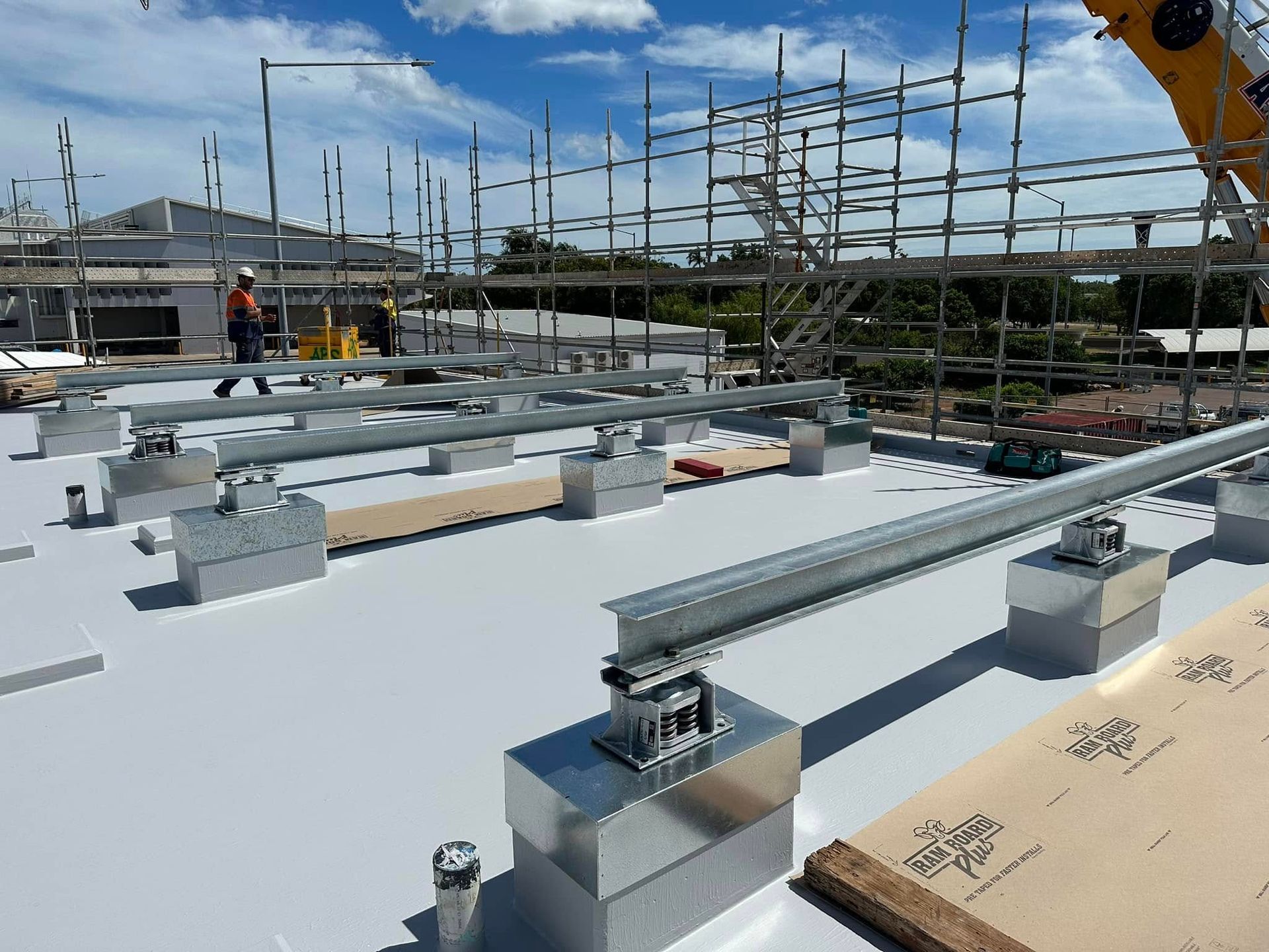 Solar panel mounting hardware on a white rooftop, with scaffolding and workers in the background on a sunny day — Great Northern Airconditioning & Mechanical Services in Berrimah, NT