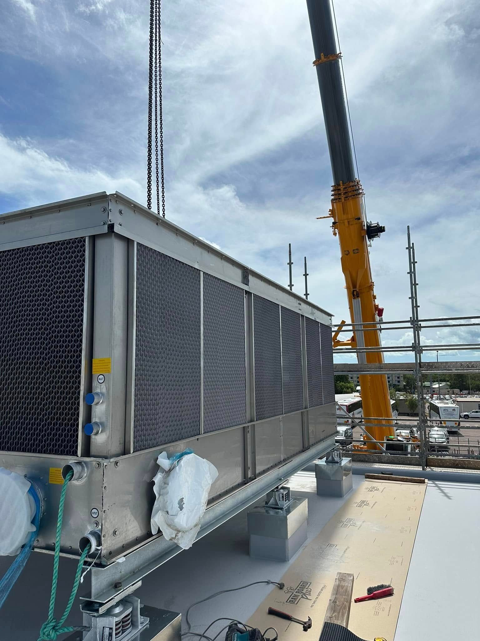 Crane lifting large air conditioning unit onto a rooftop against a cloudy sky — Great Northern Airconditioning & Mechanical Services in Berrimah, NT