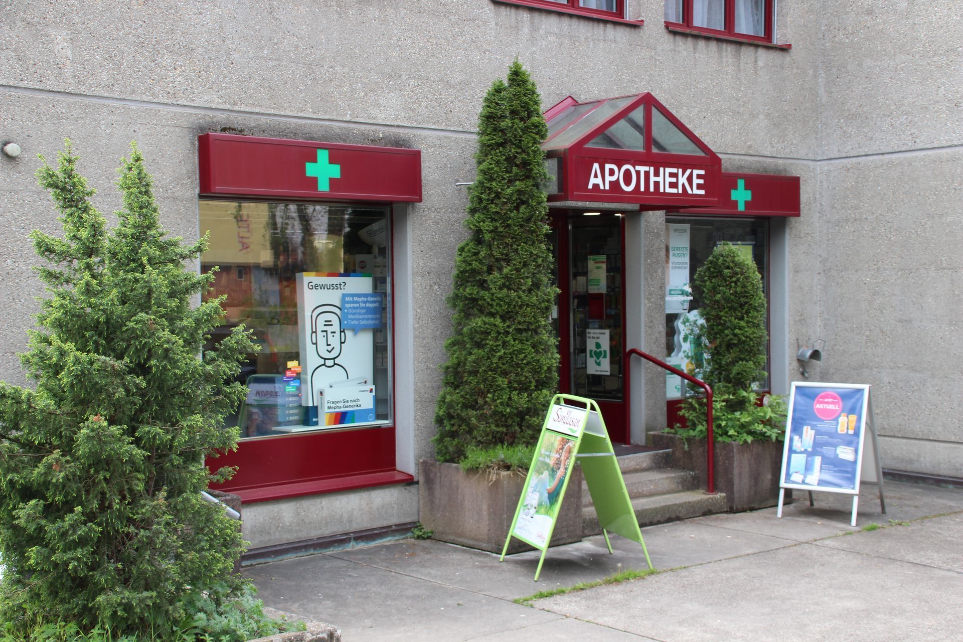 Apothekenfassade mit roter Markise, grünem Kreuz und dem Schild „APOTHEKE“.
