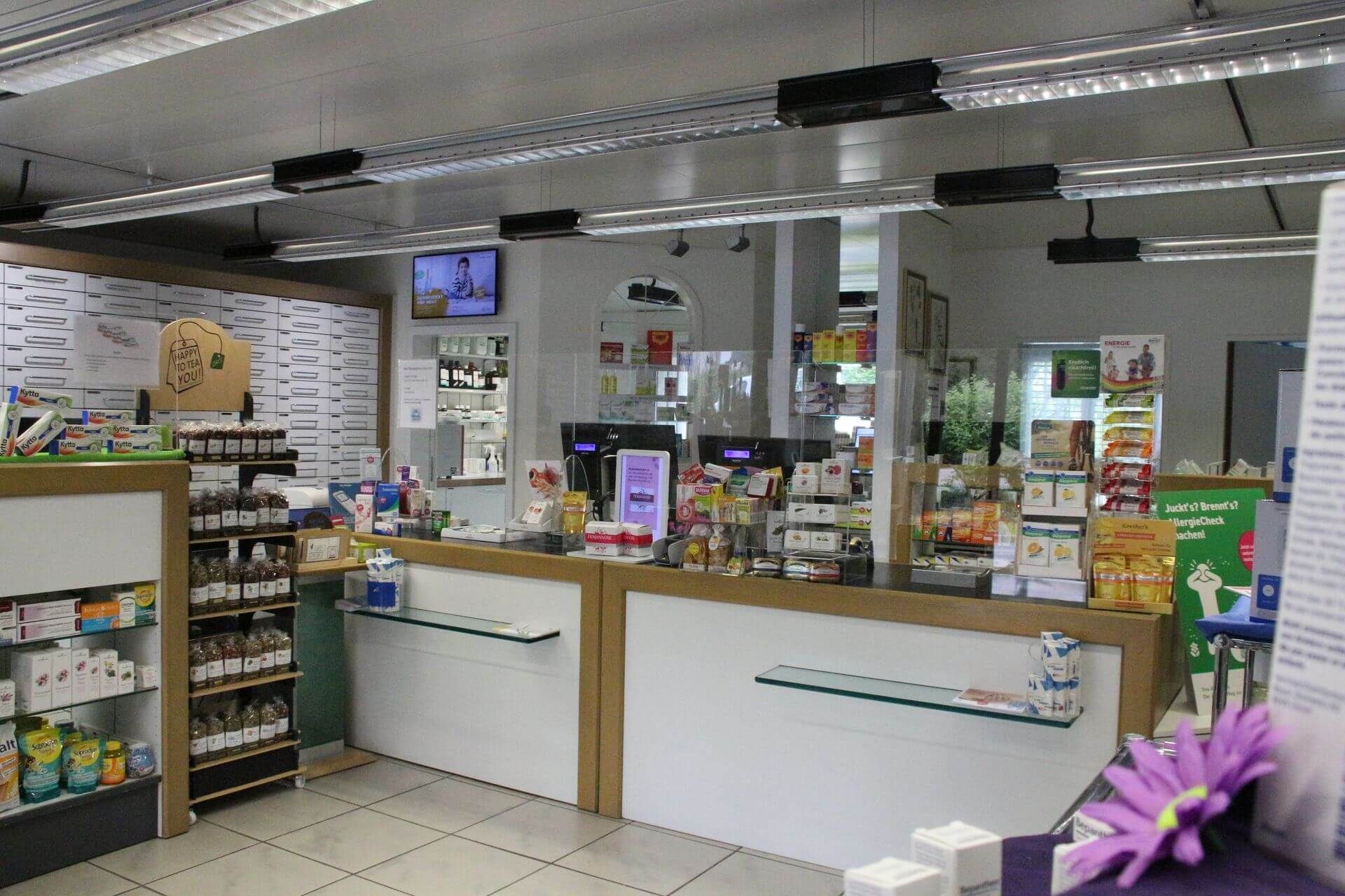 Innenansicht einer Apotheke mit Theke, Regalen voller Produkte und einem Fernsehbildschirm.