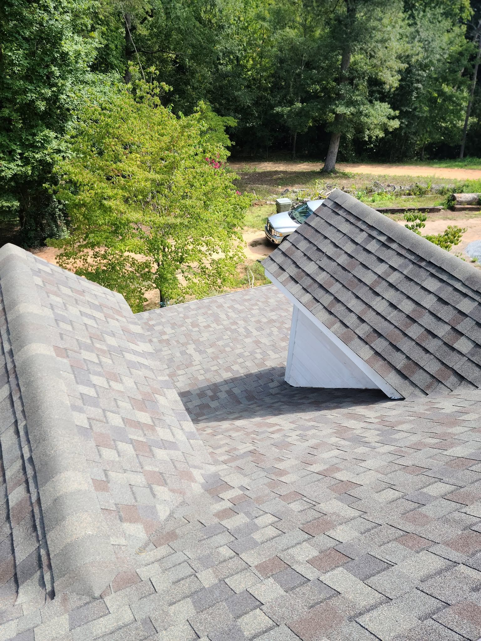 Rooftops with gray shingles overlooking trees and a grassy yard