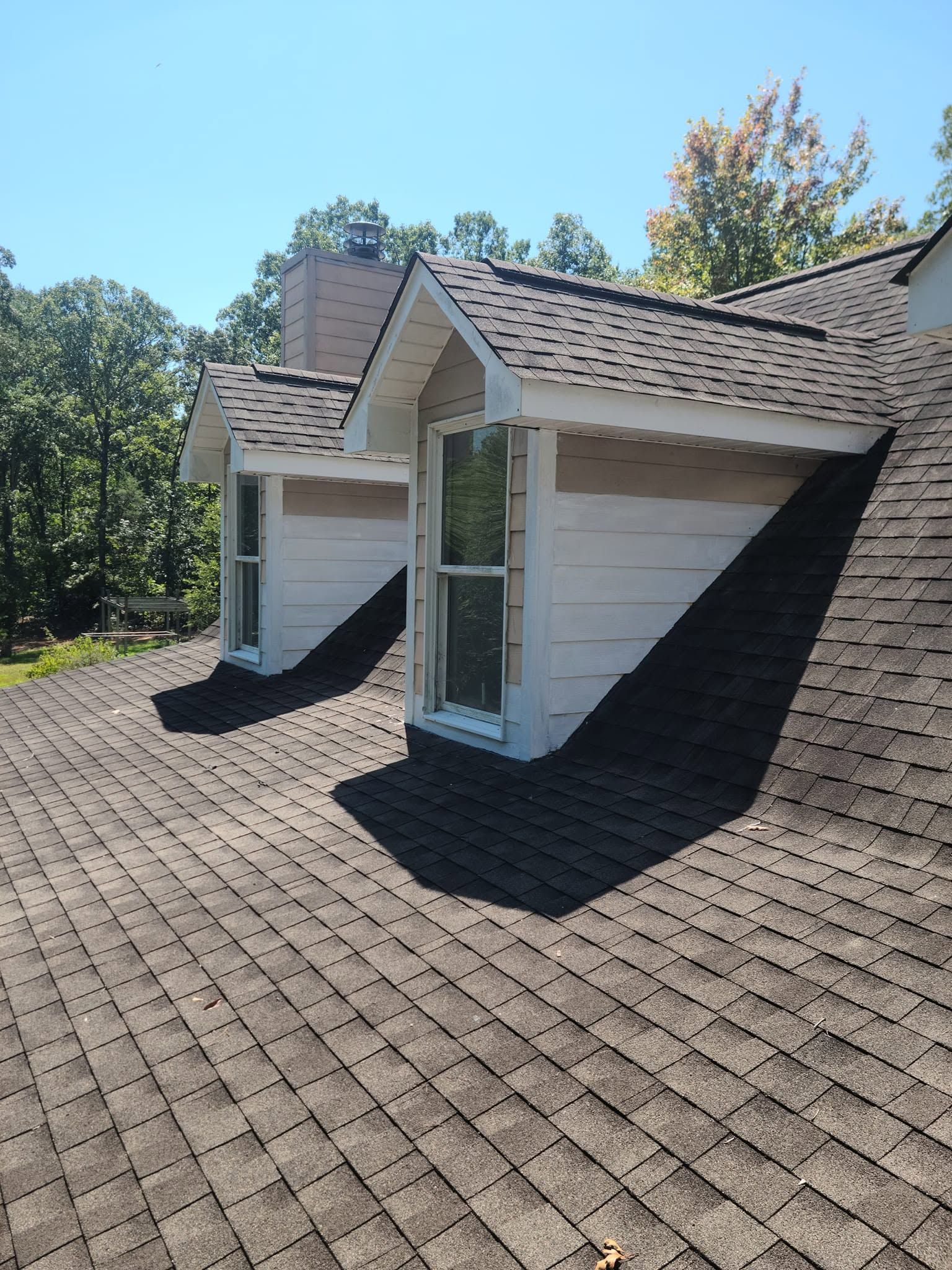 Roof with two dormer windows and white siding under a clear blue sky