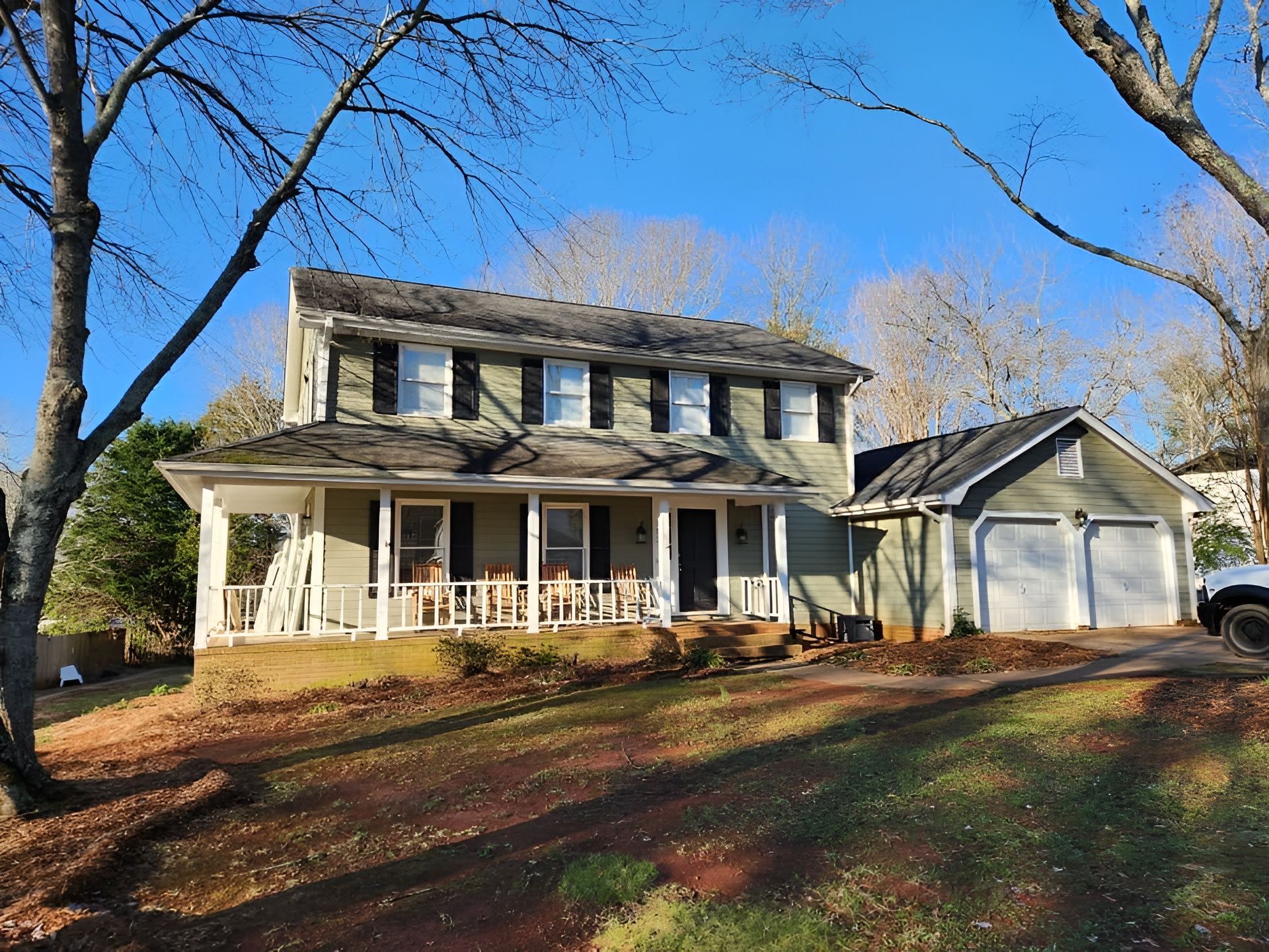 Two-story white house with a front porch and detached garage on a sunny autumn day