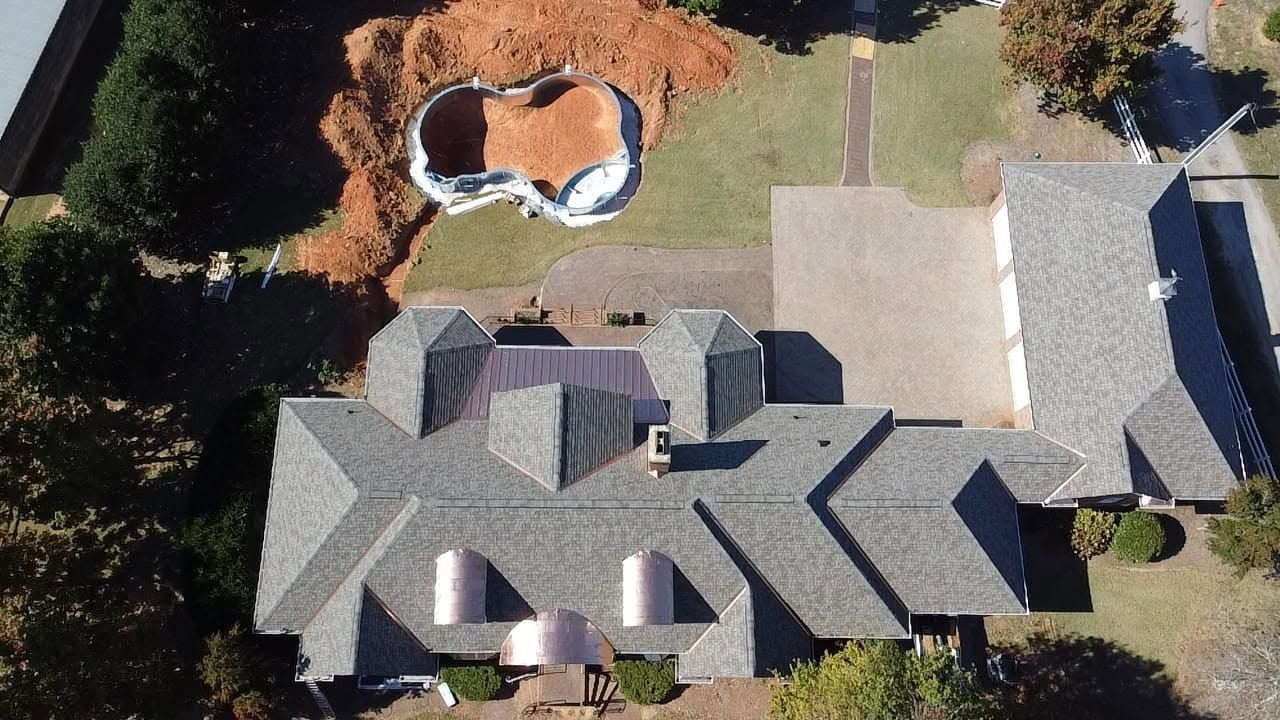 Aerial view of a house with gray roof, driveway, and backyard patio with a small pool.