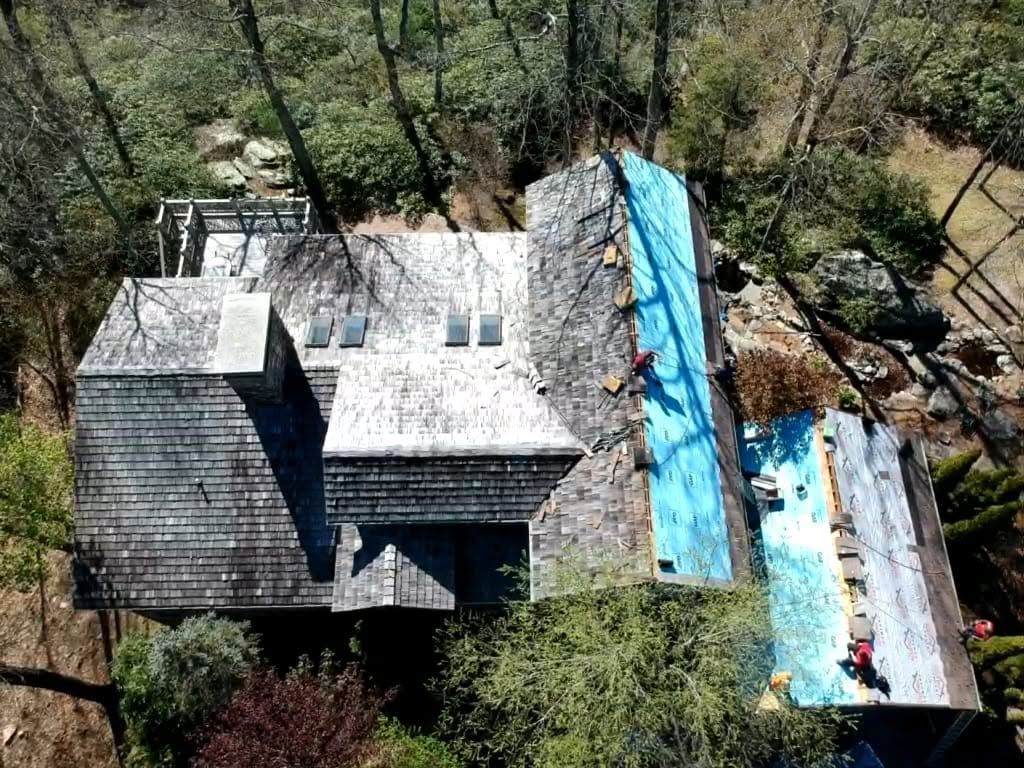 Aerial view of a house with gray and blue roofs surrounded by trees and debris