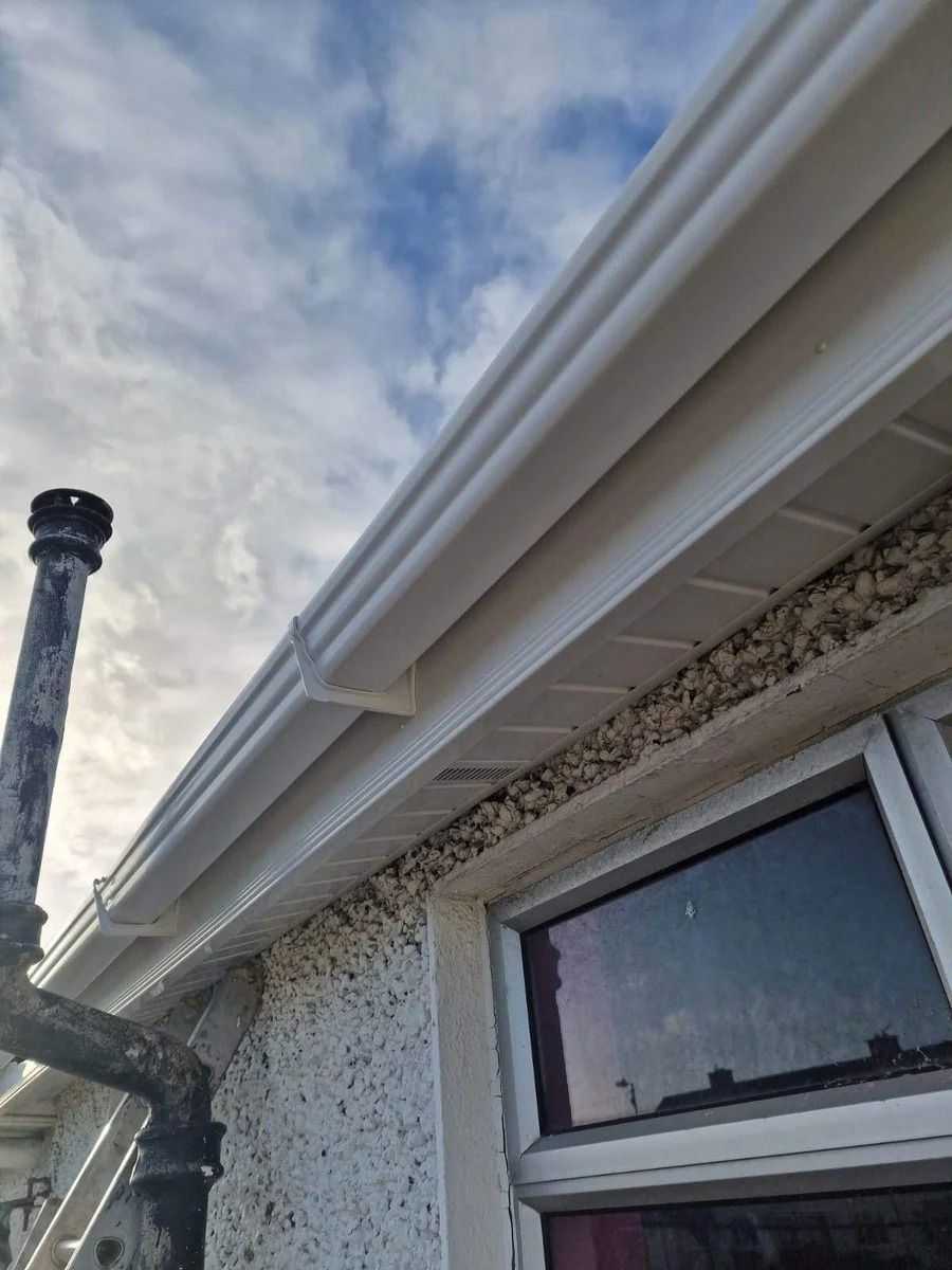 House exterior with white eaves and gutter against a cloudy sky, with a window below.