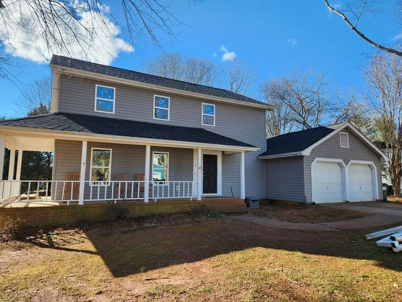 Two-story gray house with white porch and detached two-car garage under a clear blue sky
