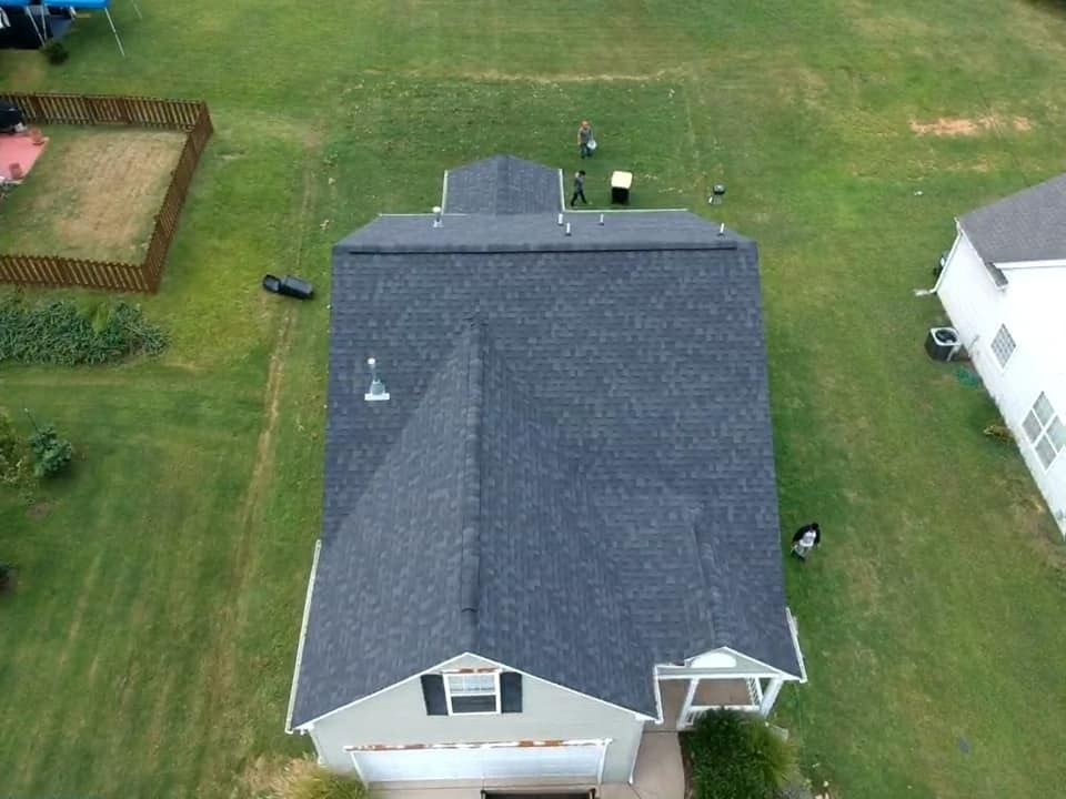 Aerial view of a house with a dark gray roof and white siding, surrounded by a green lawn.