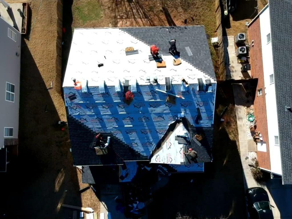 Aerial view of a house roof wrapped in blue tarp, with workers and materials on top during repairs