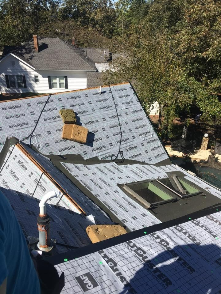 Roofing work on a house, with exposed underlayment, vents, and a ladder in the foreground.