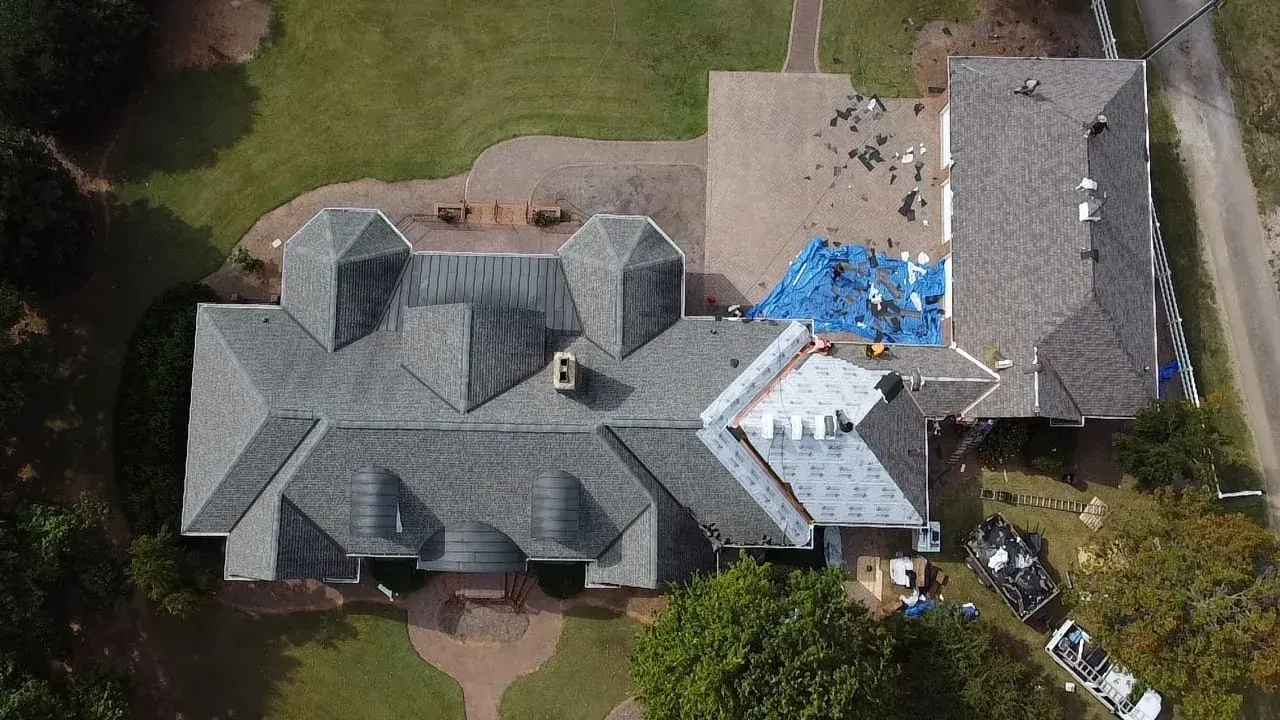 Aerial view of a house roof with storm damage and blue tarp covering a section near the right side