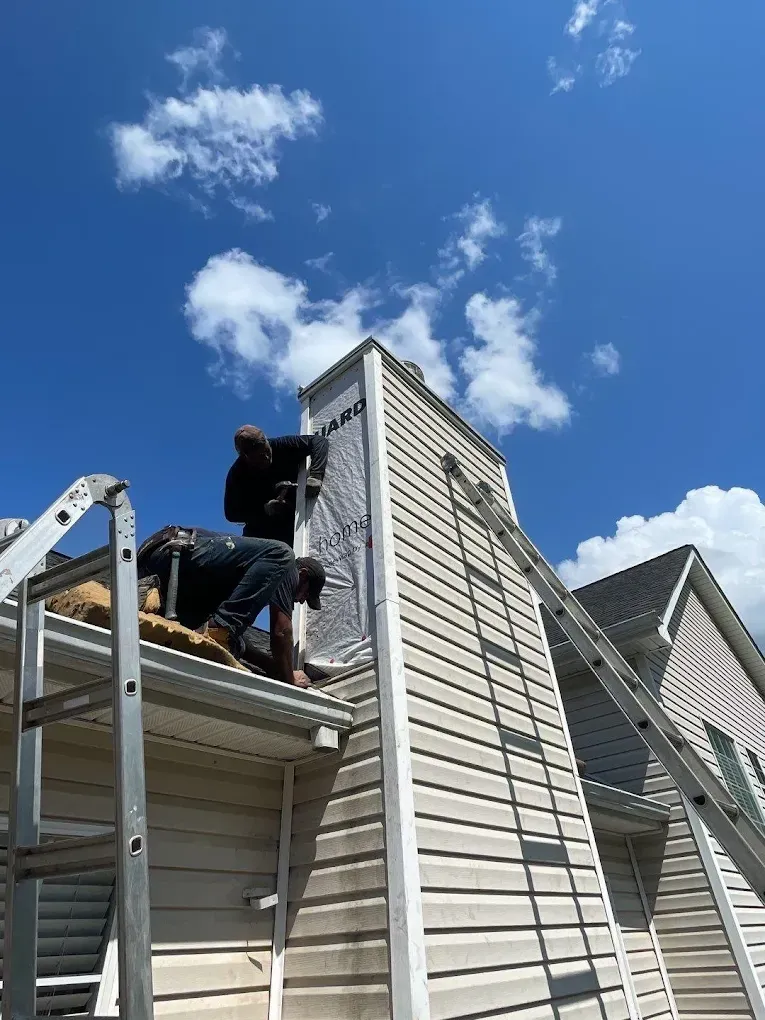 Worker on a ladder repairing light siding on a house under a blue sky