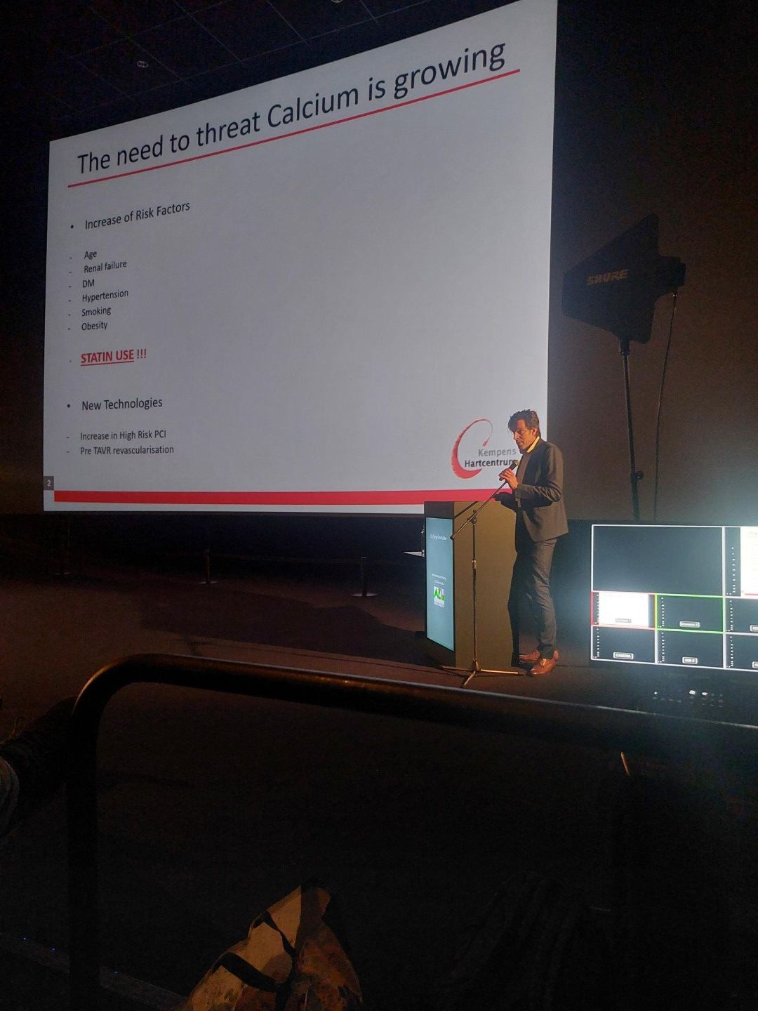 Spreker presenteert dia's over calciumgroei op een donker conferentiepodium.