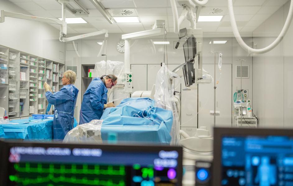 Een chirurgisch team in blauwe jassen werkt in een lichte operatiekamer met monitoren op de voorgrond.