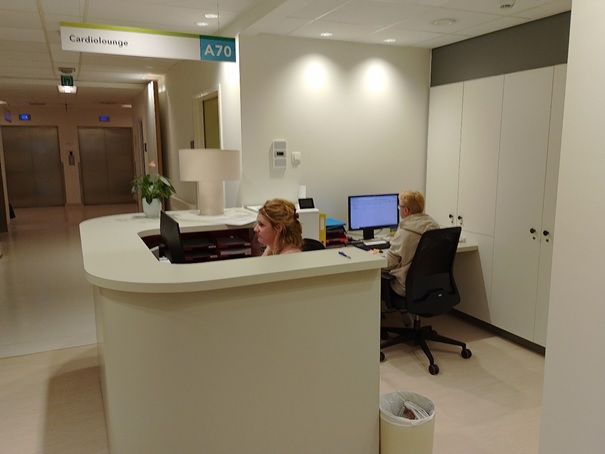 Receptiebalie in een lichte gang van de kliniek met twee medewerkers achter computers.