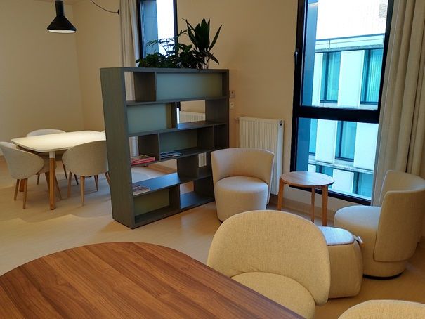 Moderne woonkamer met beige stoelen, houten planken, kleine tafels en grote ramen.