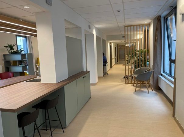 Moderne kantoorlounge met bureaus, stoelen, ramen en potplanten.