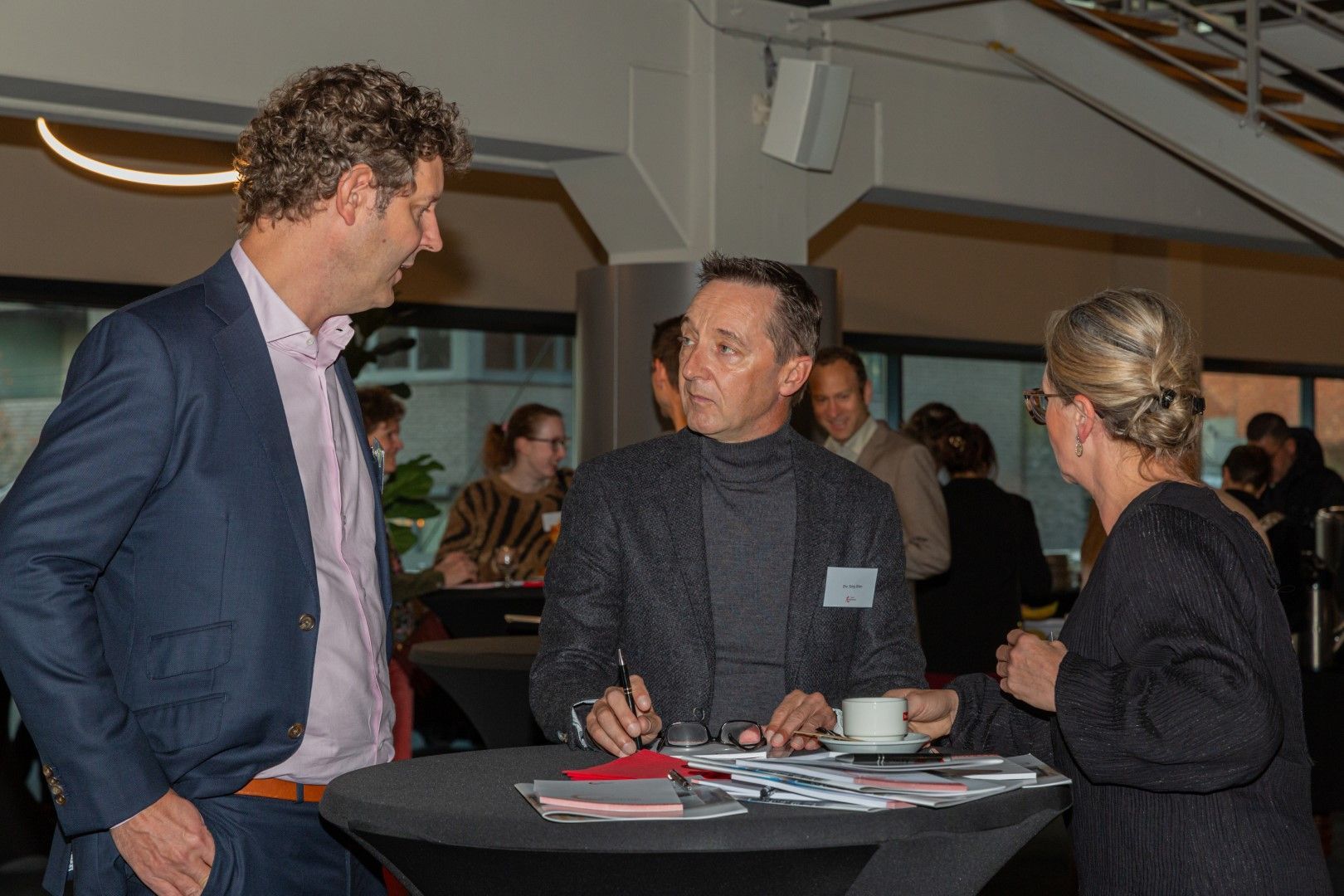 Drie mensen voeren een gesprek aan een cocktailtafel tijdens een netwerkevenement.