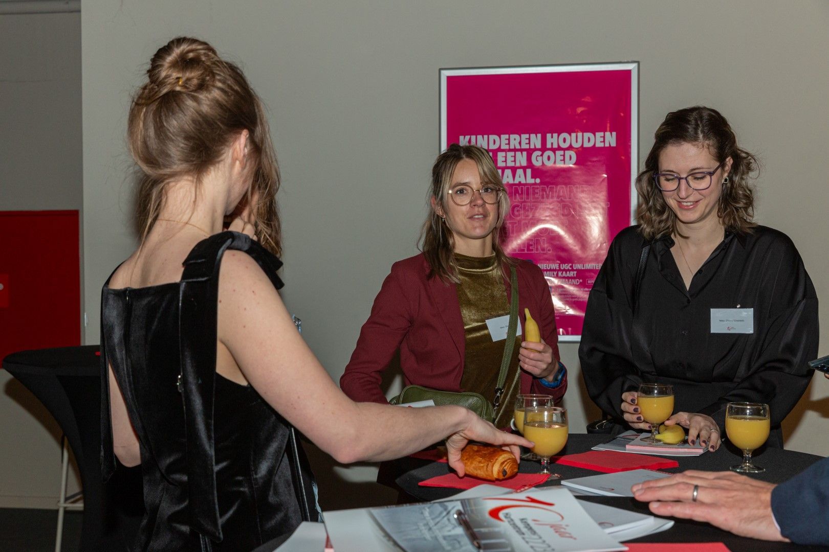 Mensen die met elkaar praten aan een tafel met drankjes en brochures in een vergaderomgeving.