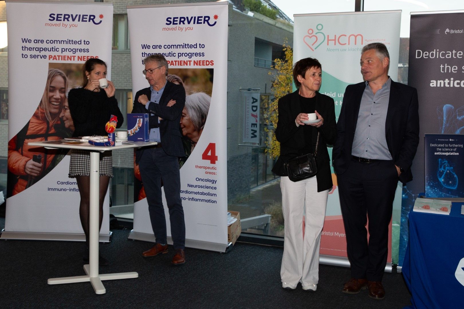 Mensen praten bij een beursstand met SERVIER-banners en displaytafels.