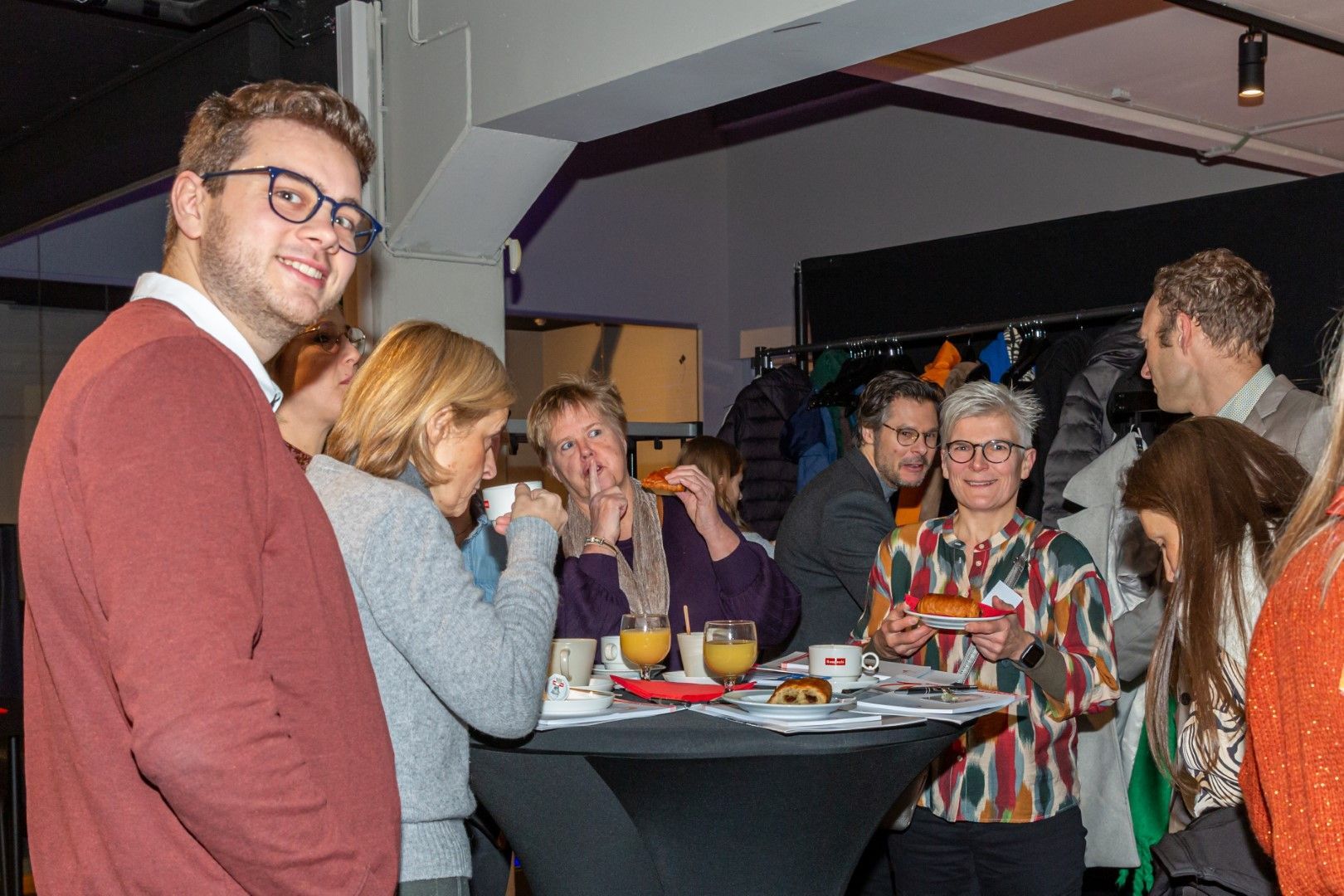 Mensen die gezellig met elkaar praten rond een hoge cocktailtafel tijdens een levendige bijeenkomst binnenshuis.