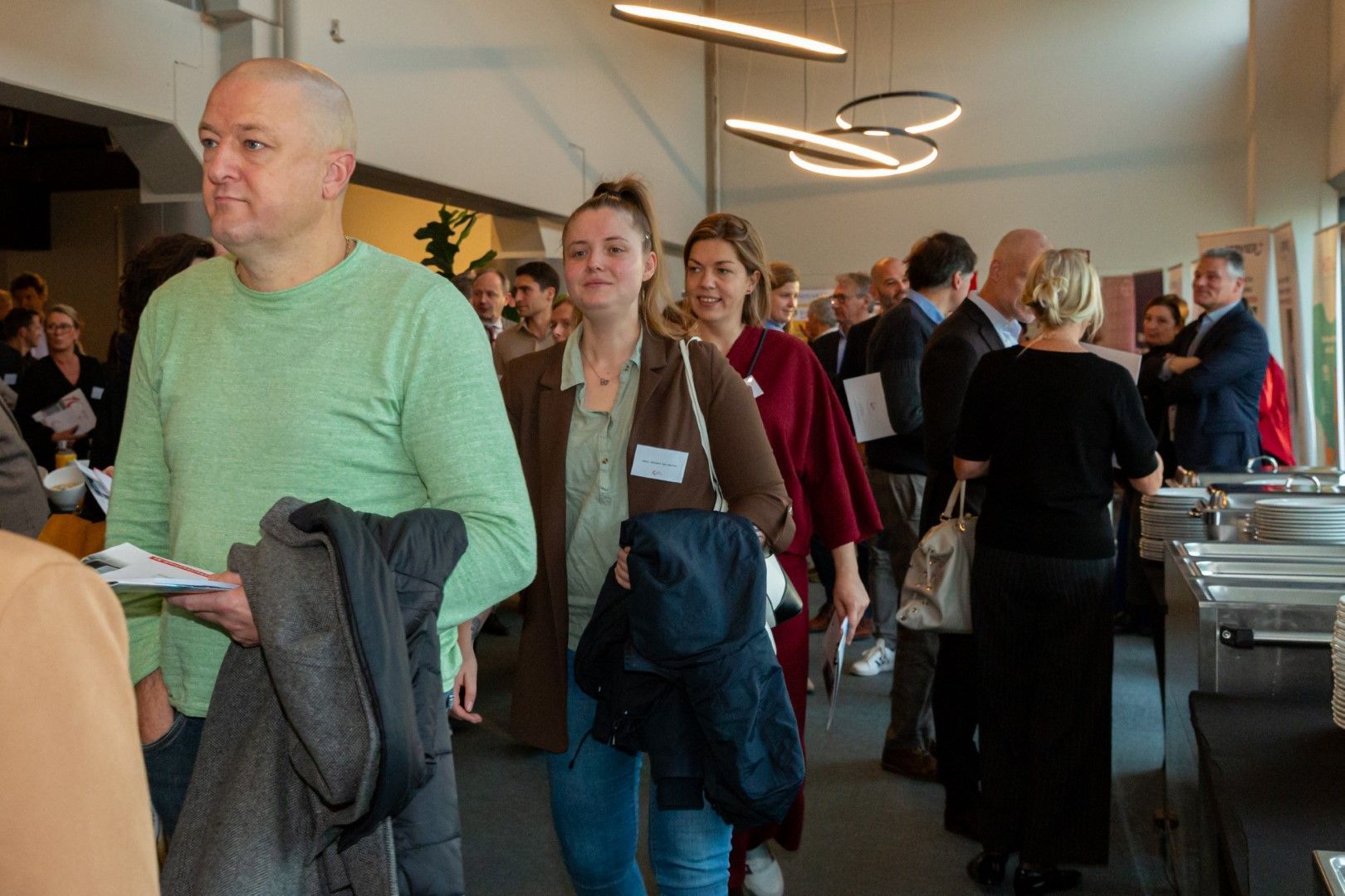 Een drukke ontvangsthal met mensen die staan te praten bij een buffet.