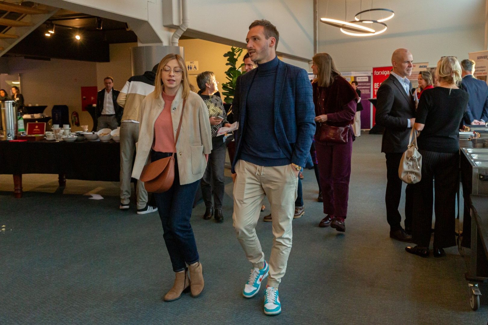 Twee mensen lopen door de lobby van een hotel, met gasten die zich op de achtergrond mengen.