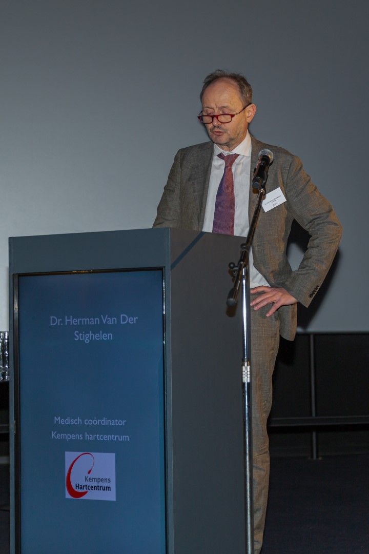 Een man, gekleed in pak en stropdas, spreekt vanaf een podium met een microfoon.