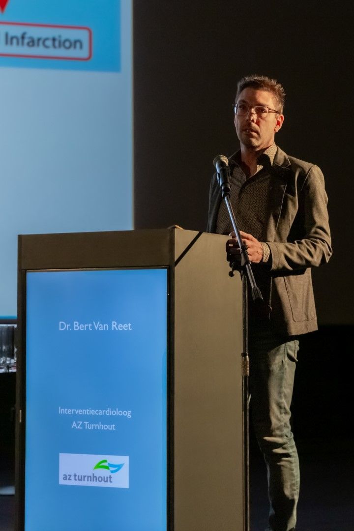 Spreker achter een podium die een presentatie geeft, met op de achtergrond een dia waarop