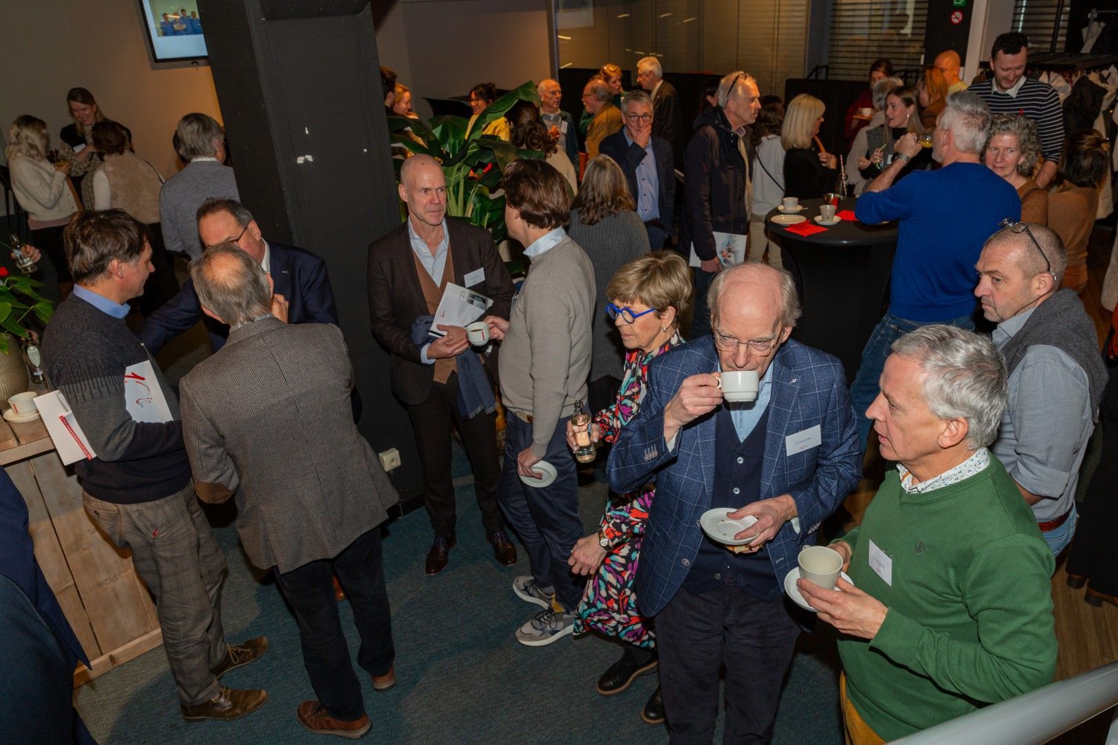 Mensen die met elkaar praten en drankjes vasthouden tijdens een drukbezochte bijeenkomst binnenshuis.
