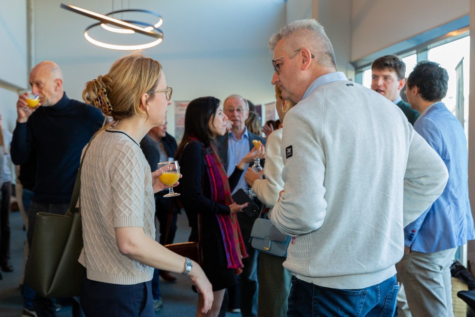 Mensen die gezellig met elkaar praten tijdens een netwerkevenement in een lichte ruimte, met drankjes in de hand en in casual kleding.