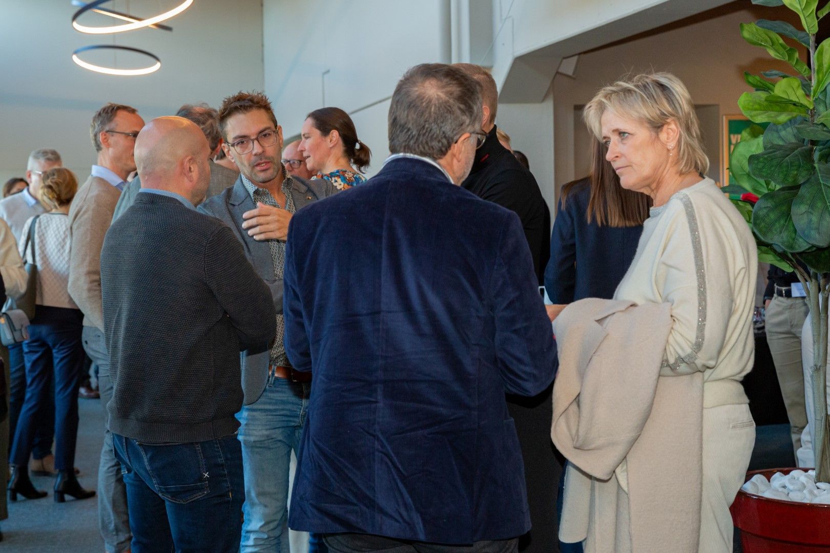 Mensen die zich mengen onder elkaar tijdens een evenement binnenshuis en een praatje maken bij een bar met planten en een moderne inrichting.