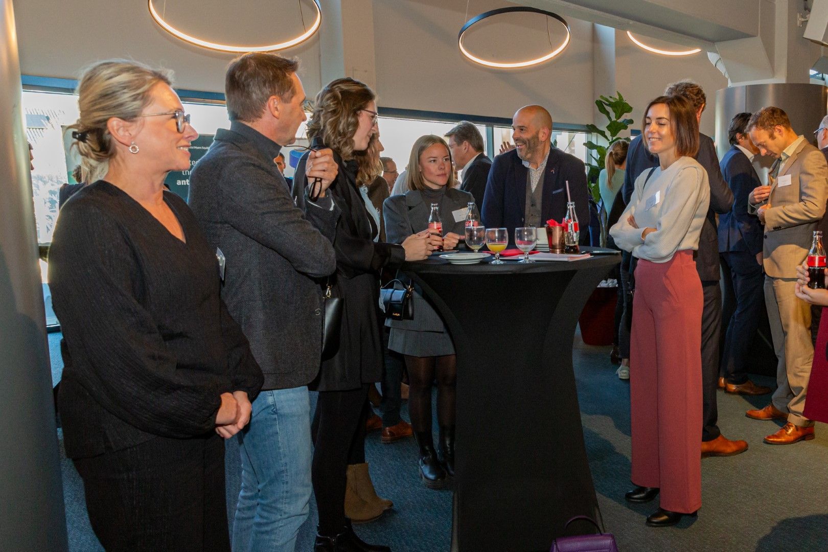 Mensen die zich mengen tijdens een cocktailreceptie rond een hoge tafel in een moderne lounge.