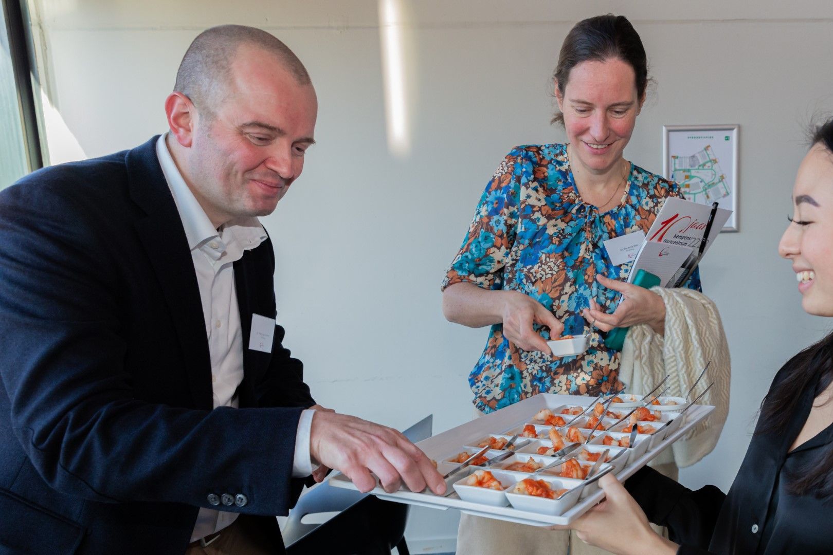 Mensen serveren gebak op schalen in een lichte, gezellige bijeenkomst binnenshuis.