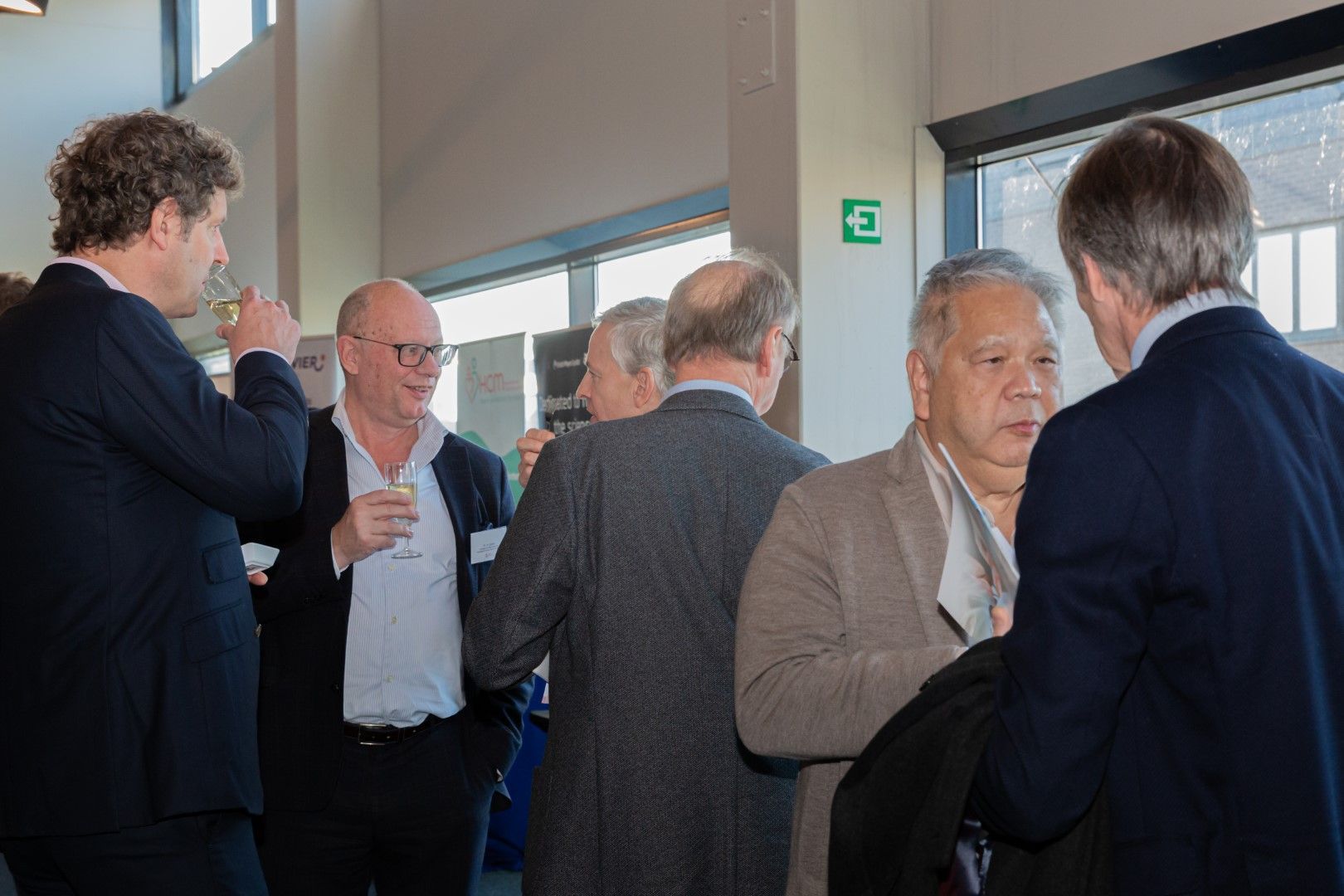 In een lichte, overdekte lobby bij grote ramen voeren verschillende mensen een gesprek.