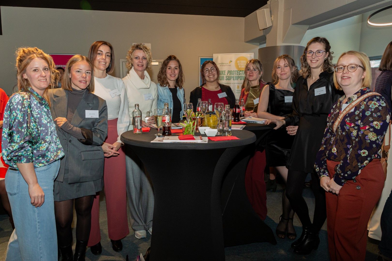 Een groep mensen staat rond een cocktailtafel tijdens een gezellige bijeenkomst binnenshuis.